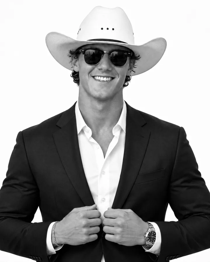Black-and-white portrait of Ty, founder of Project Valley Revamp, smiling in a white cowboy hat, sunglasses, dark suit and open-collar white shirt.